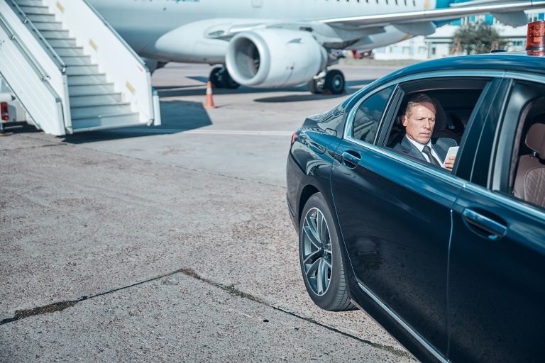 Man in suit on phone in luxury car at airport tarmac.