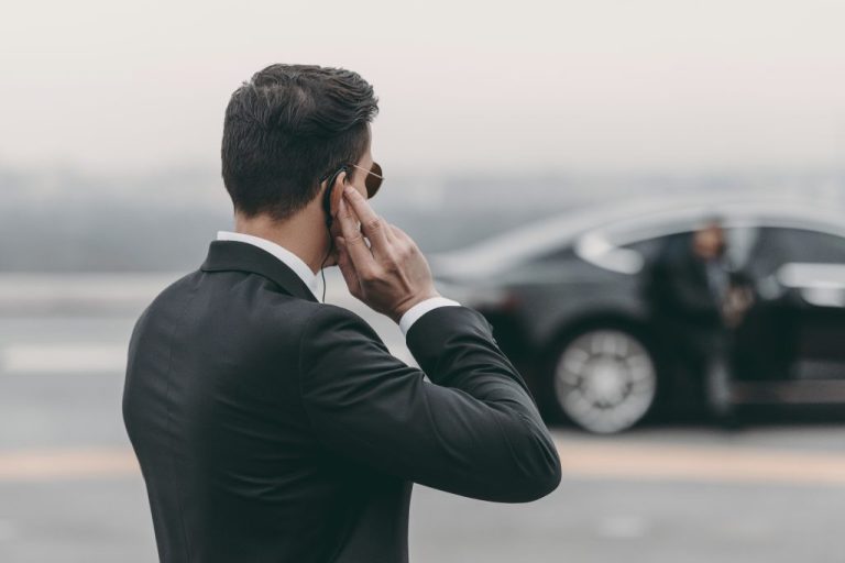 Bodyguard in suit with earpiece near luxury car.