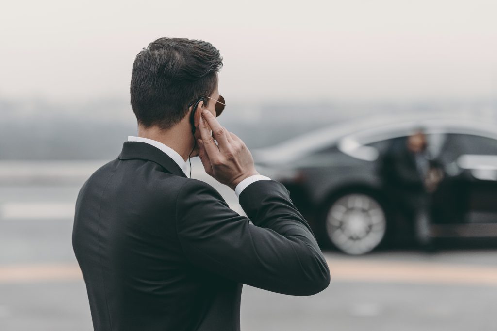 Bodyguard in suit with earpiece near luxury car.